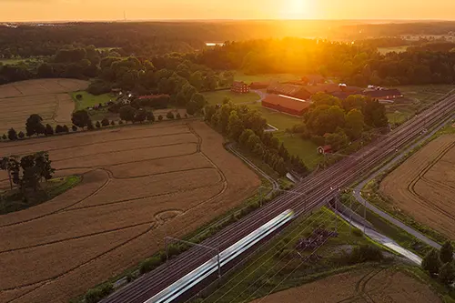 Tåg åker genom svenskt landskap i solnedgång